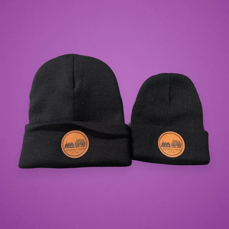 Two black beanies, adult and kids size, with round leather farm-logo patches